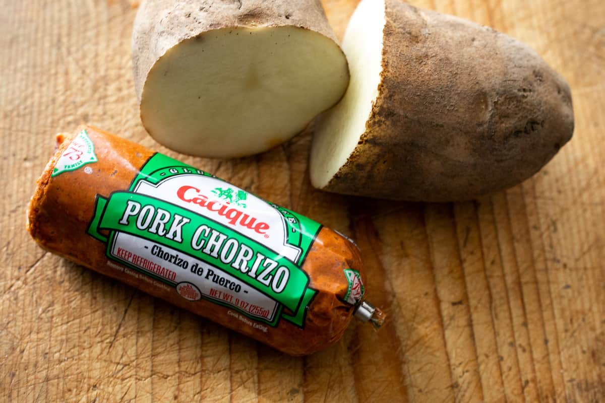 halved russet potato and a tube of Cacique brand pork chorizo on a wooden surface. 