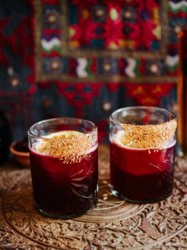 two glasses of hibiscus margaritas on an etched wooden table.