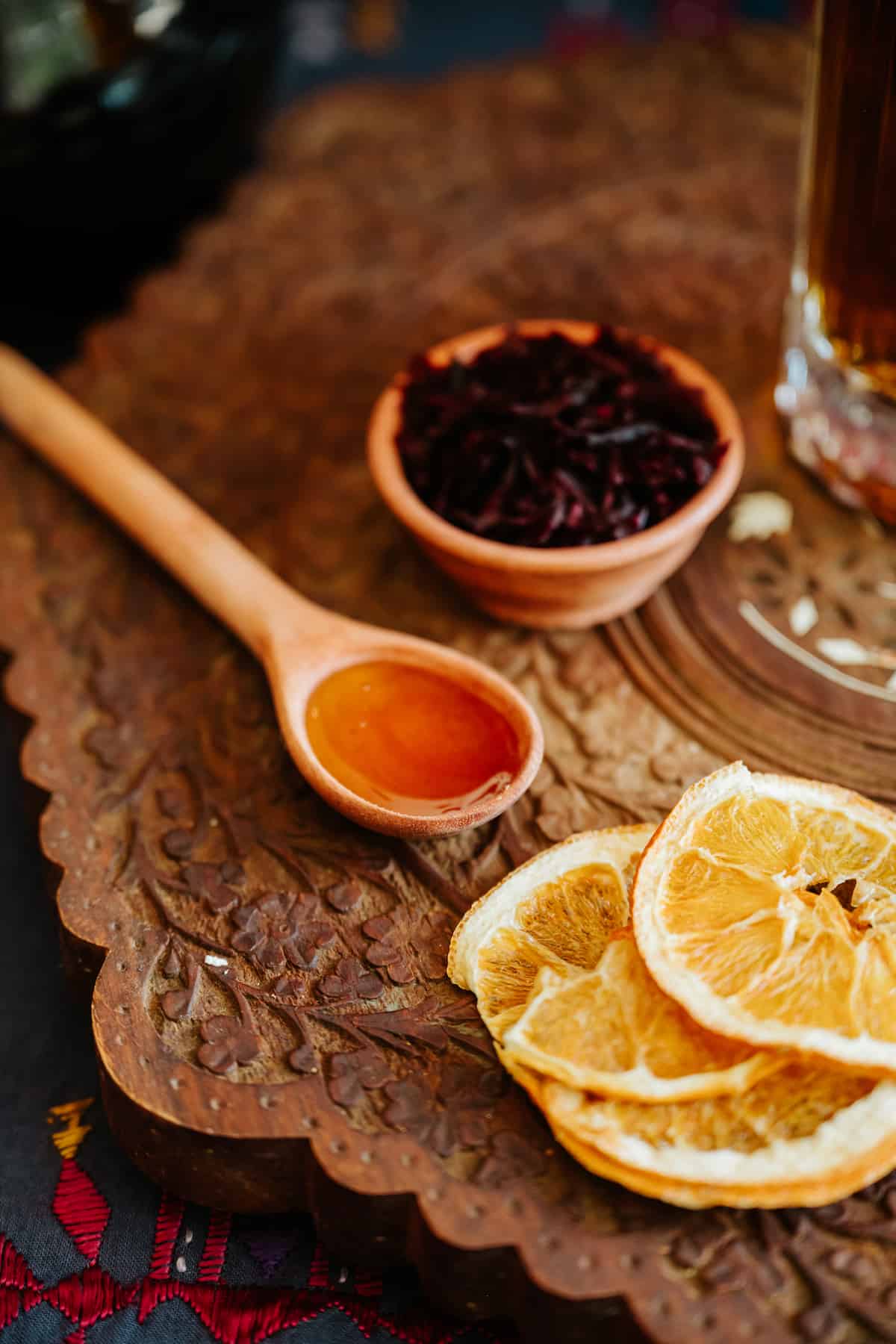 closeup on dried orange slices, a wooden spoonful of agave, and a small terracotta bowl of hibiscus flowers.