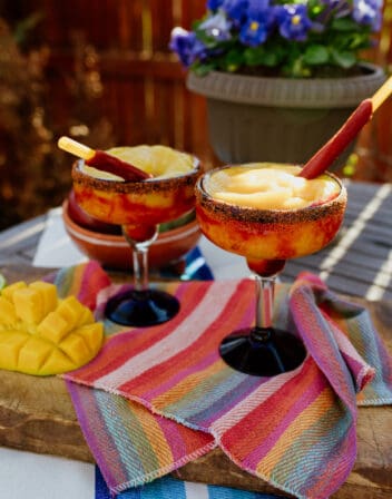 two margarita glasses filled with frozen mangonada margarita and garnished with tarugos straws.