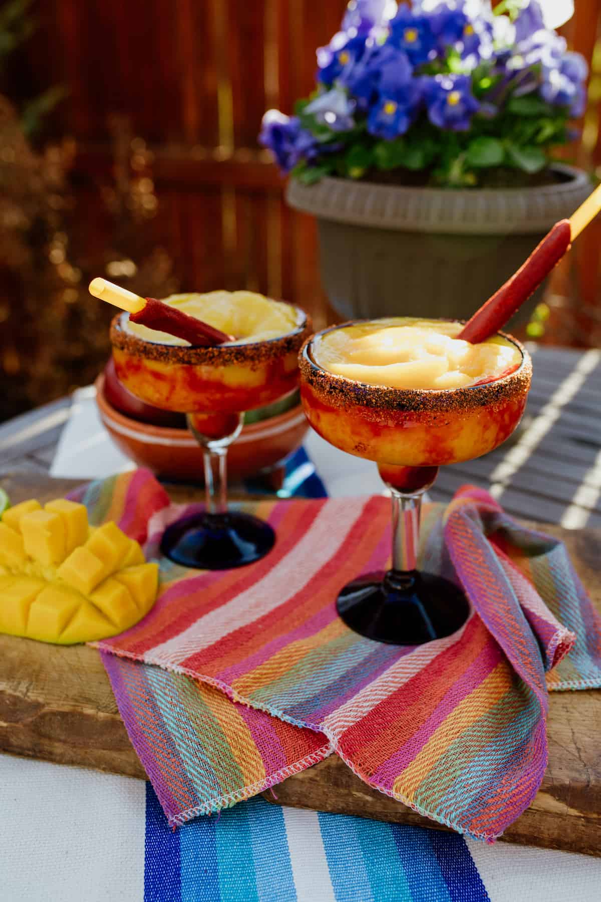 closeup on two glasses of frozen mangonada margaritas outside with the sun shining. 