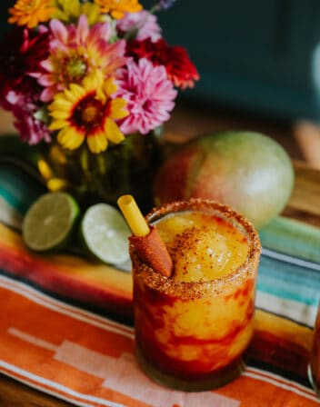 45 degree angle shot of a rocks glass rimmed in tajin and filled with mangonada swirled with chamoy and garnished with a tamarind straw.