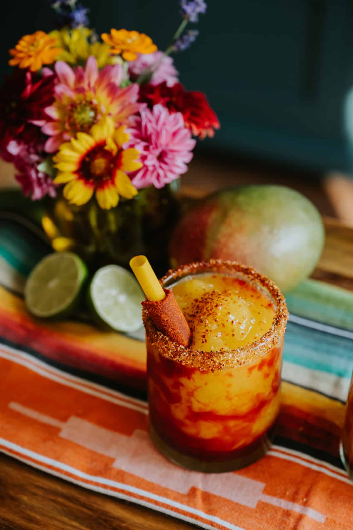 45 degree angle shot of a rocks glass rimmed in tajin and filled with mangonada swirled with chamoy and garnished with a tamarind straw. 