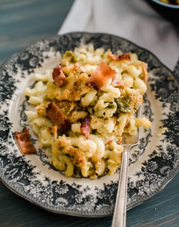 spicy poblano, hatch green chile, and bacon mac and cheese on a black and white dinner plate with a silver fork.