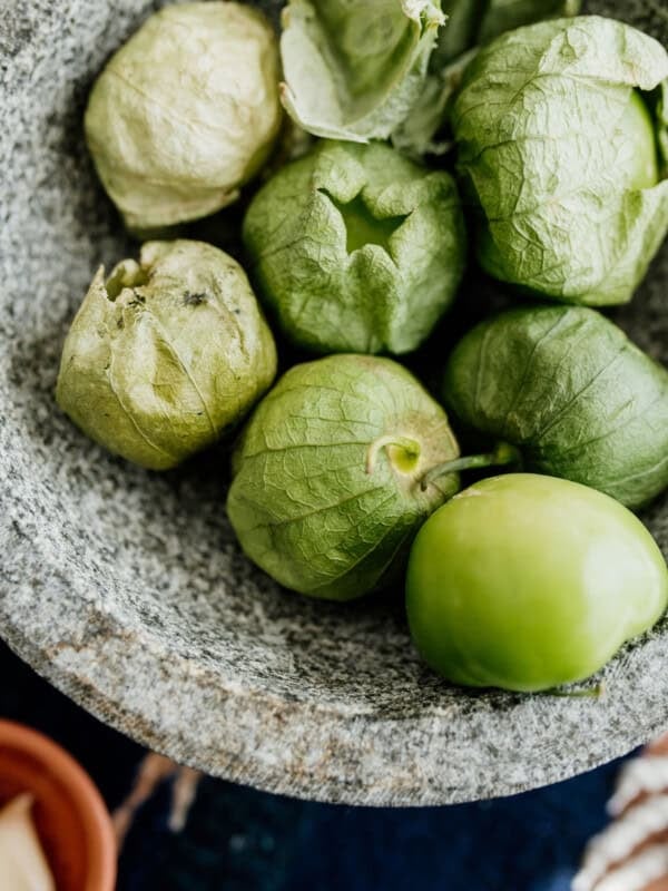 molcajete filled with tomatillos, some of which are still in the husks and some which are bare.