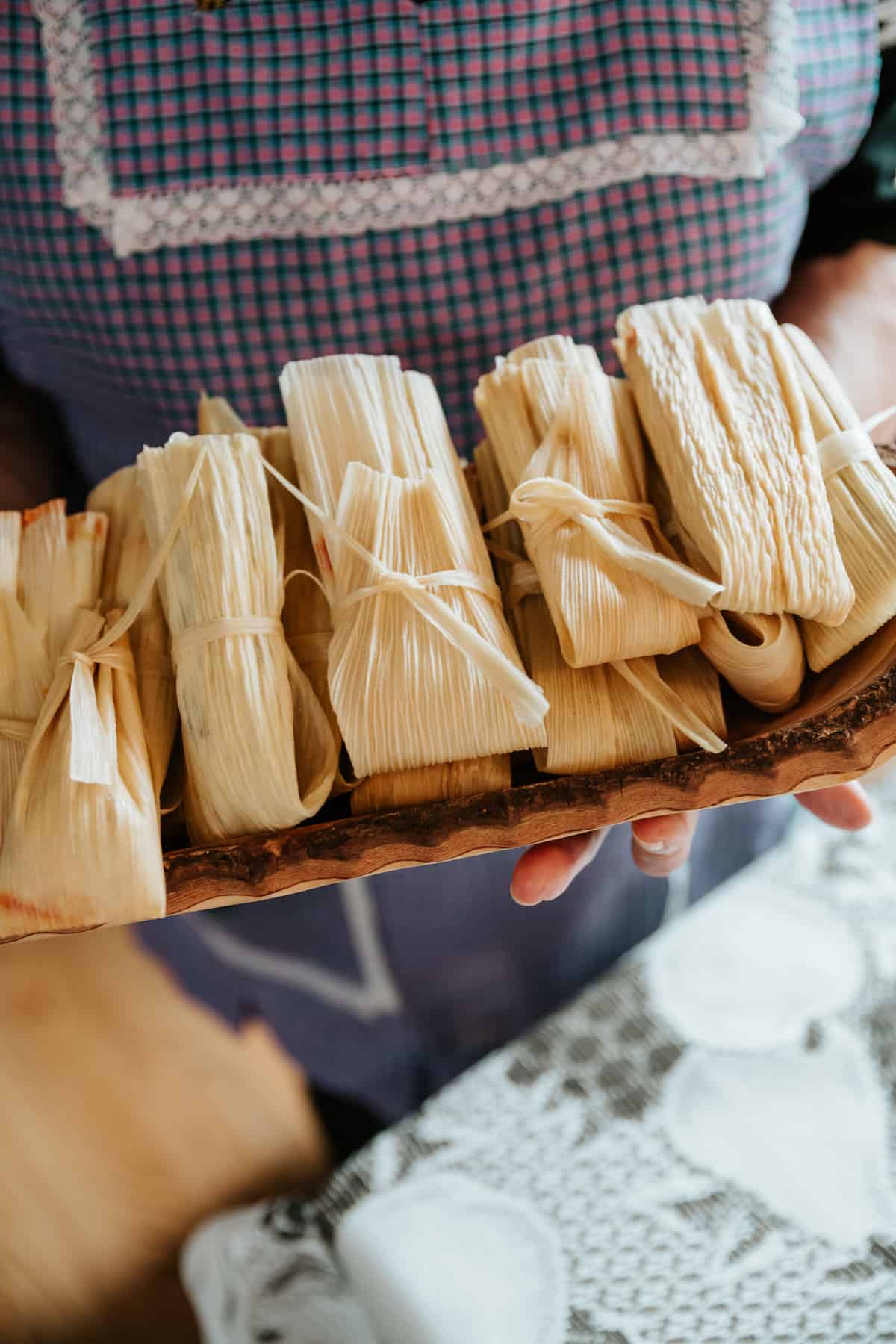 hands holding a hand-carved wooden tray filled with wrapped tamales.