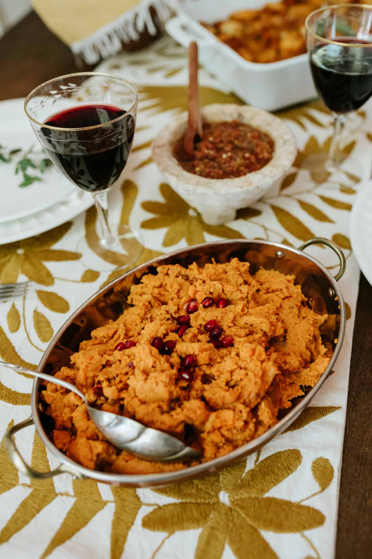 holiday table runner on a wooden table with a large silver oval serving platter filled with savory mashed chipotle sweet potatoes.