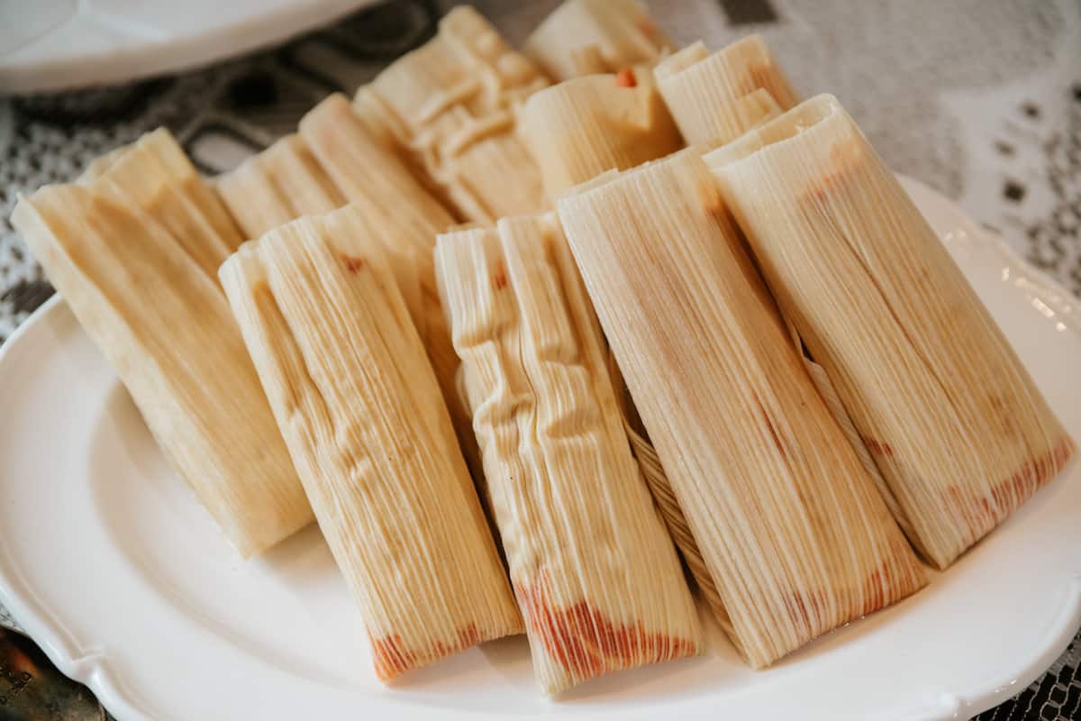 oblong white serving plate of steamed pork tamales rojos in their husks. 