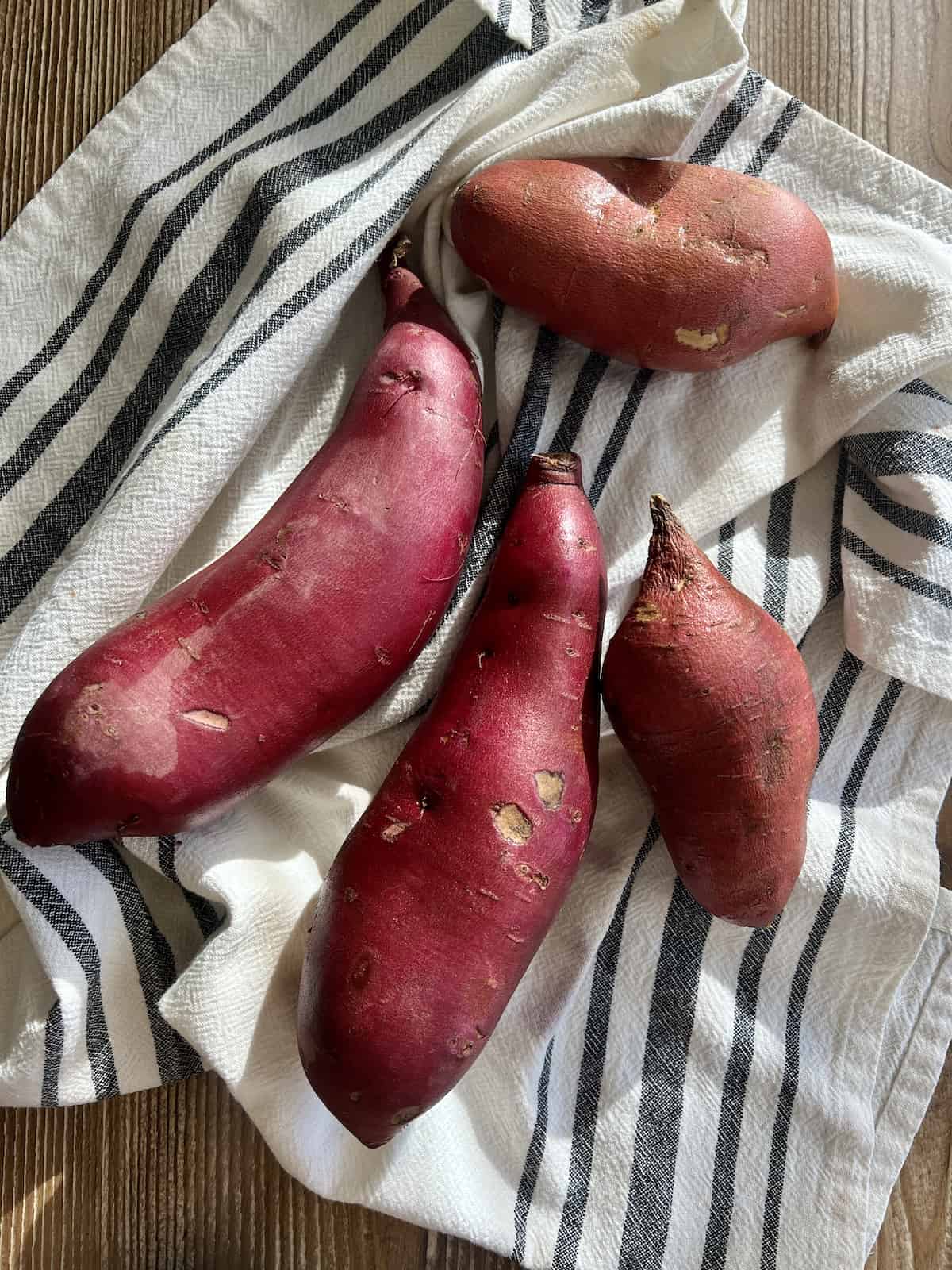 3 cooked sweet potatoes resting on a clean kitchen towel ready to be peeled.