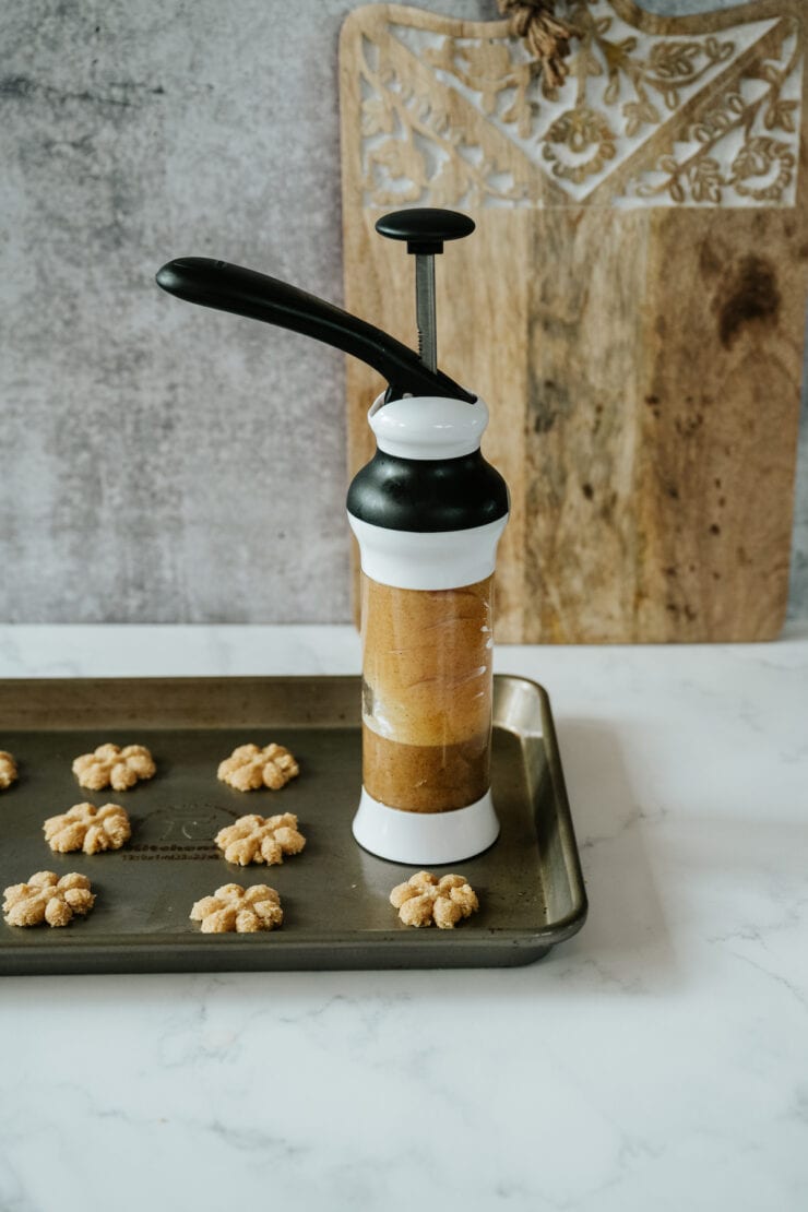 Cookie press with freshly pressed biscochos arranged on a baking sheet, ready to bake.