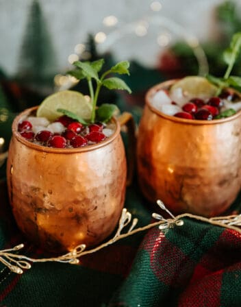 two copper moscow mule cups filled with tequila mules garnished with cranberries.