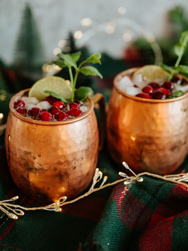 two copper moscow mule cups filled with tequila mules garnished with cranberries.