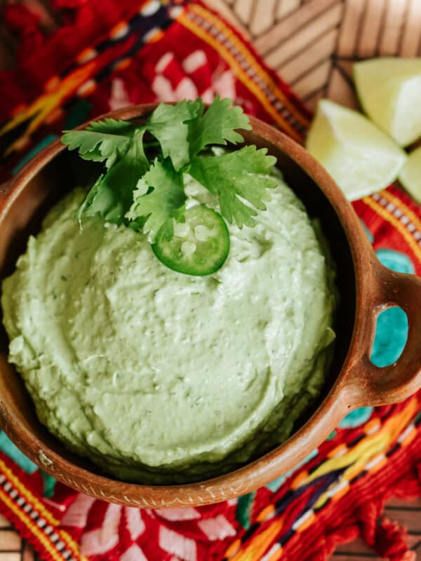 flat lay closeup shot of a bowl of avocado lime crema on a brightly colored tablecloth.