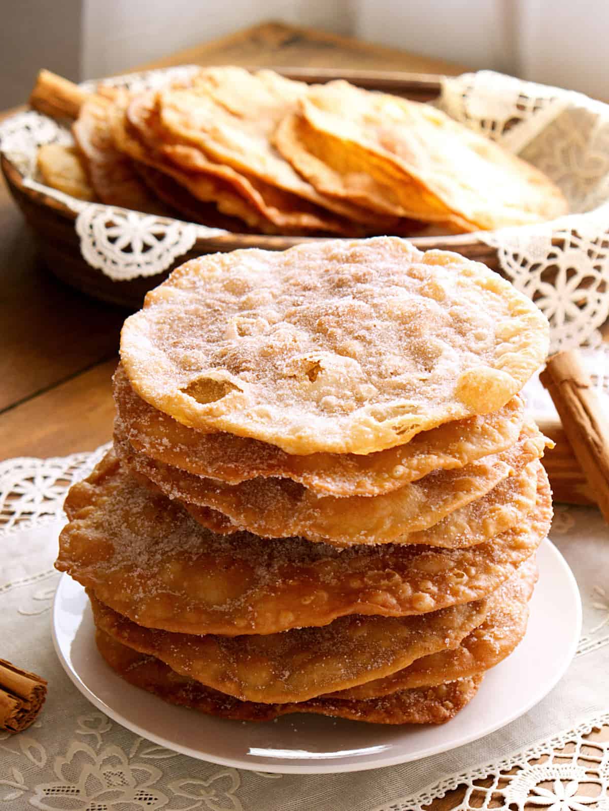 stack of golden, crisp Mexican buñuelos on a wooden table with lace doilies.