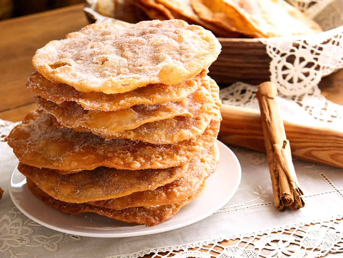 hero shot of a serving plate of Mexican buñuelos on a white doily with a canela stick and a French style rolling pin.