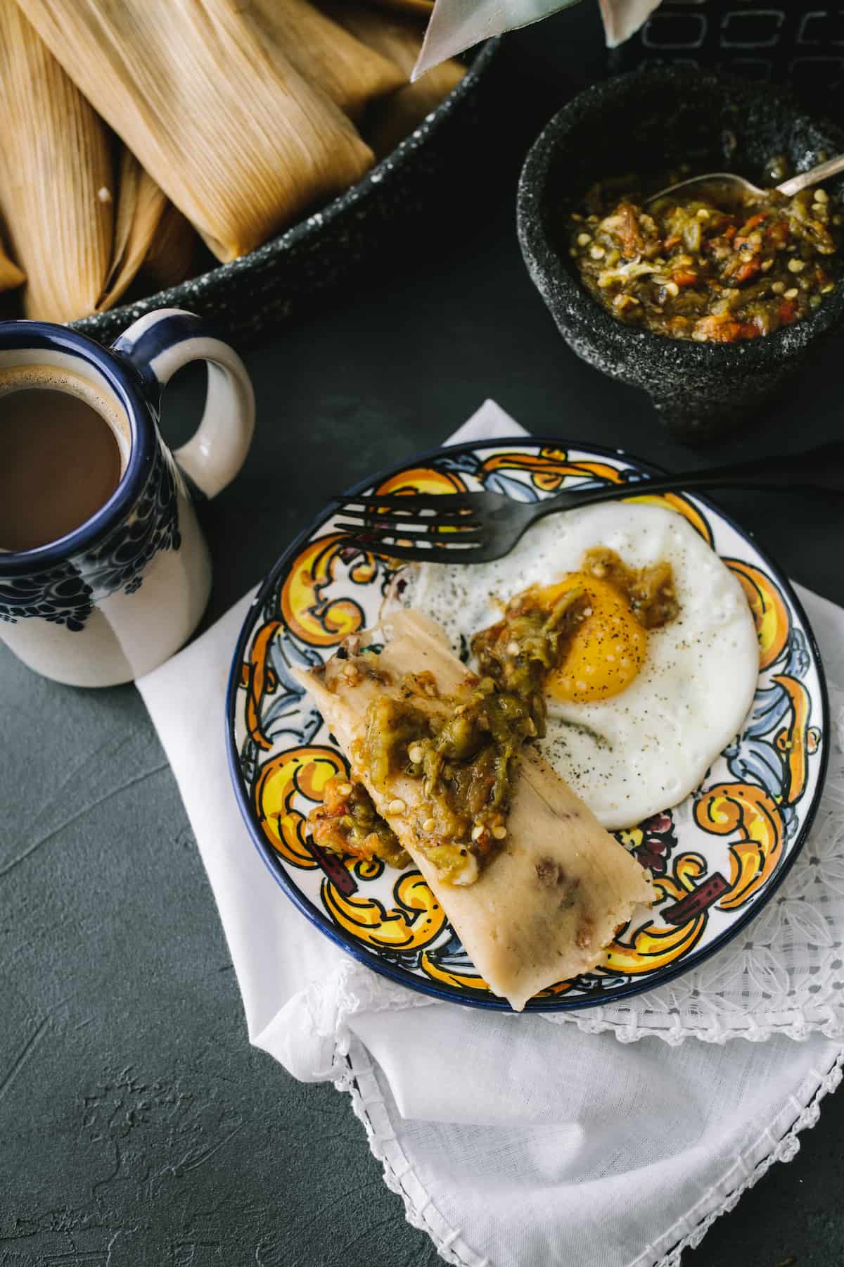 instant pot steamed pork tamale on a colorful hand-painted plate topped with extra roasted green chiles and served with a sunny side up egg.