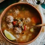 flat lay shot of a bowl of caldo de albondigas topped with extra roasted green chiles.