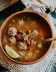 flat lay shot of a bowl of caldo de albondigas topped with extra roasted green chiles.