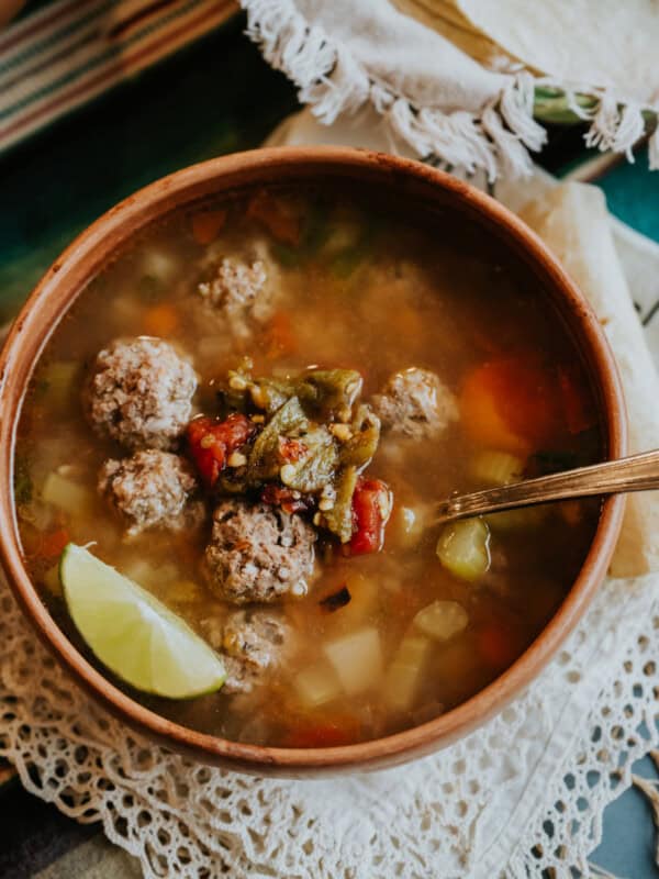 flat lay shot of a bowl of caldo de albondigas topped with extra roasted green chiles.