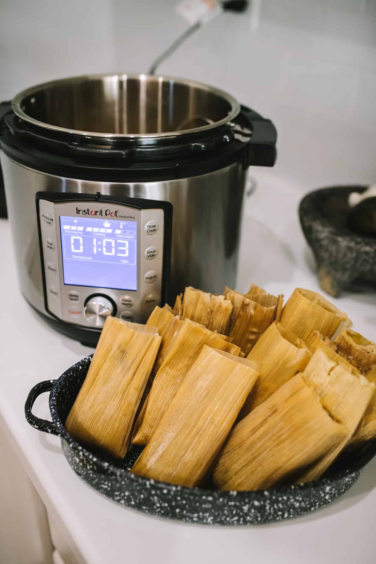 Instant Pot Pork and Roasted Green Chile Tamales after steaming in an earthenware dish next to an instant pot.