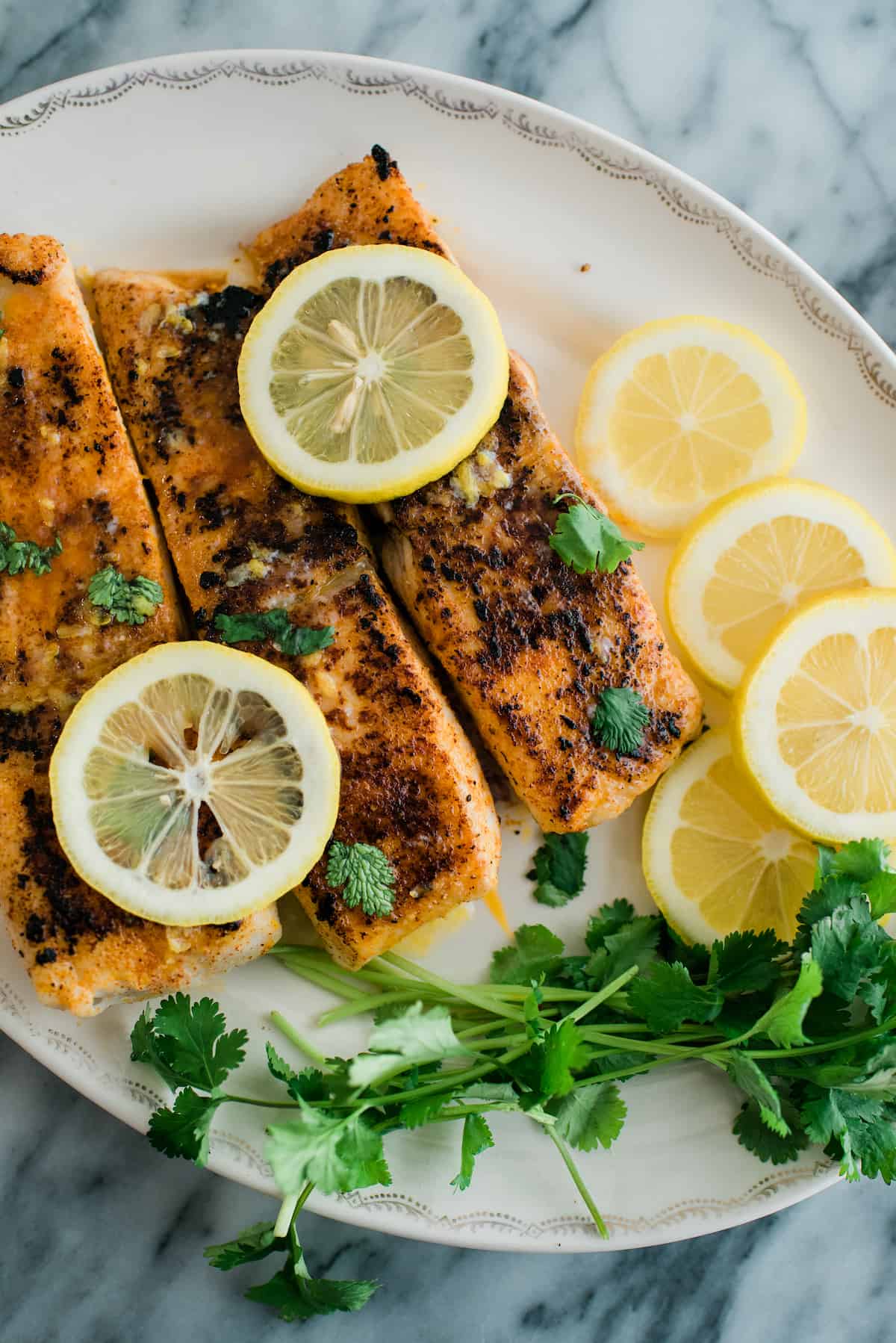 Lemon Butter Cod served with lemons and herbs on a white serving tray.