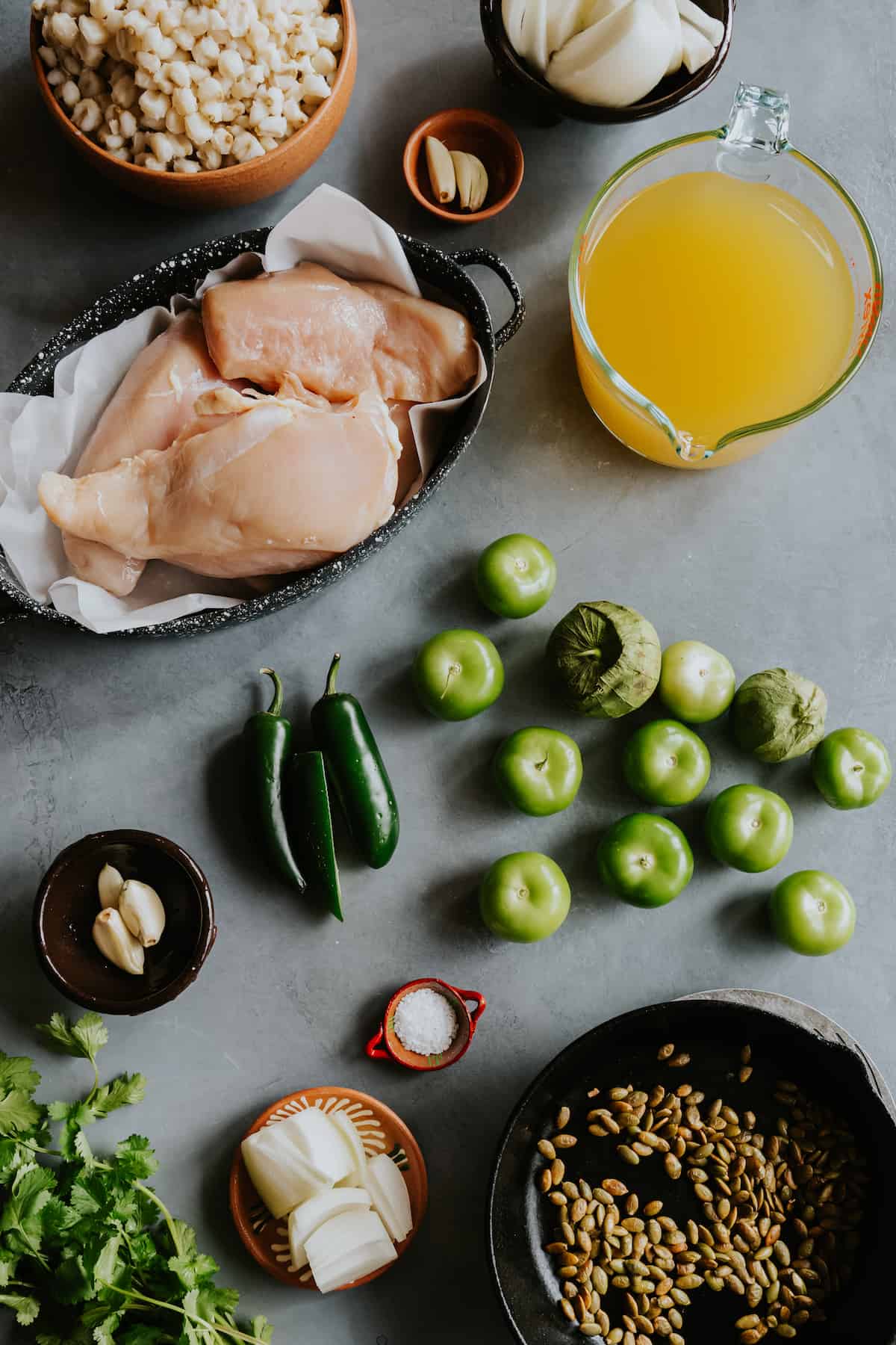 flat lay shot of the ingredients needed to make pozole verde with chicken measured out on a grey table.