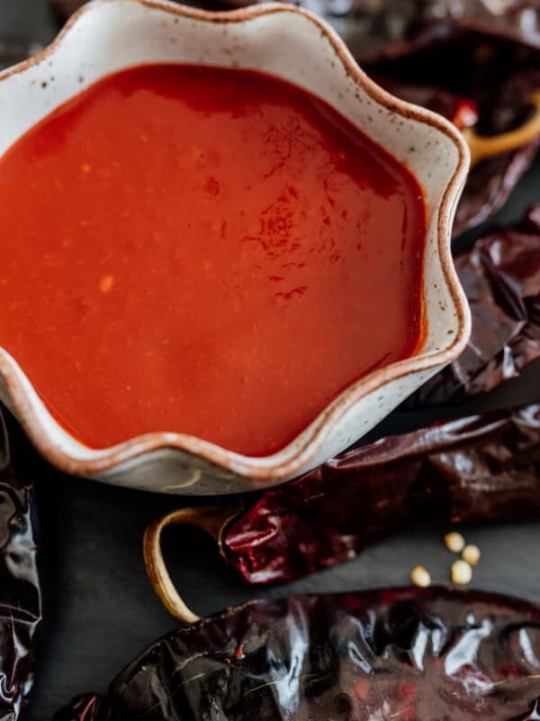 Red Chile sauce in a bowl surrounded by dried New Mexico Chile pods.