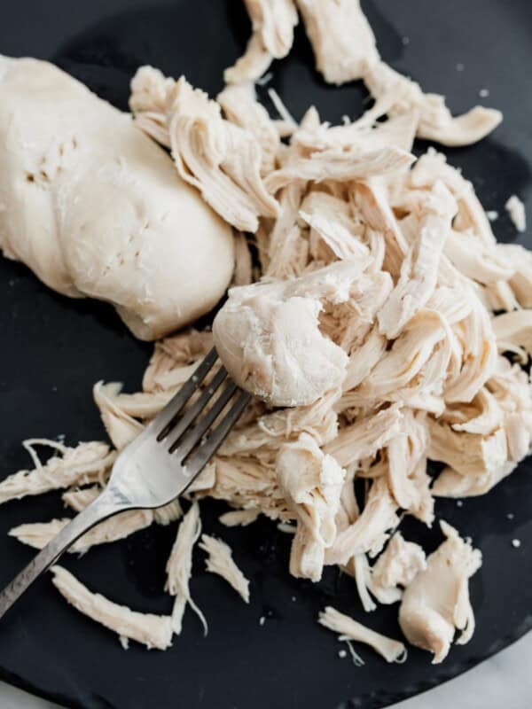 Poaching chicken breast with a metal fork on a dark plate