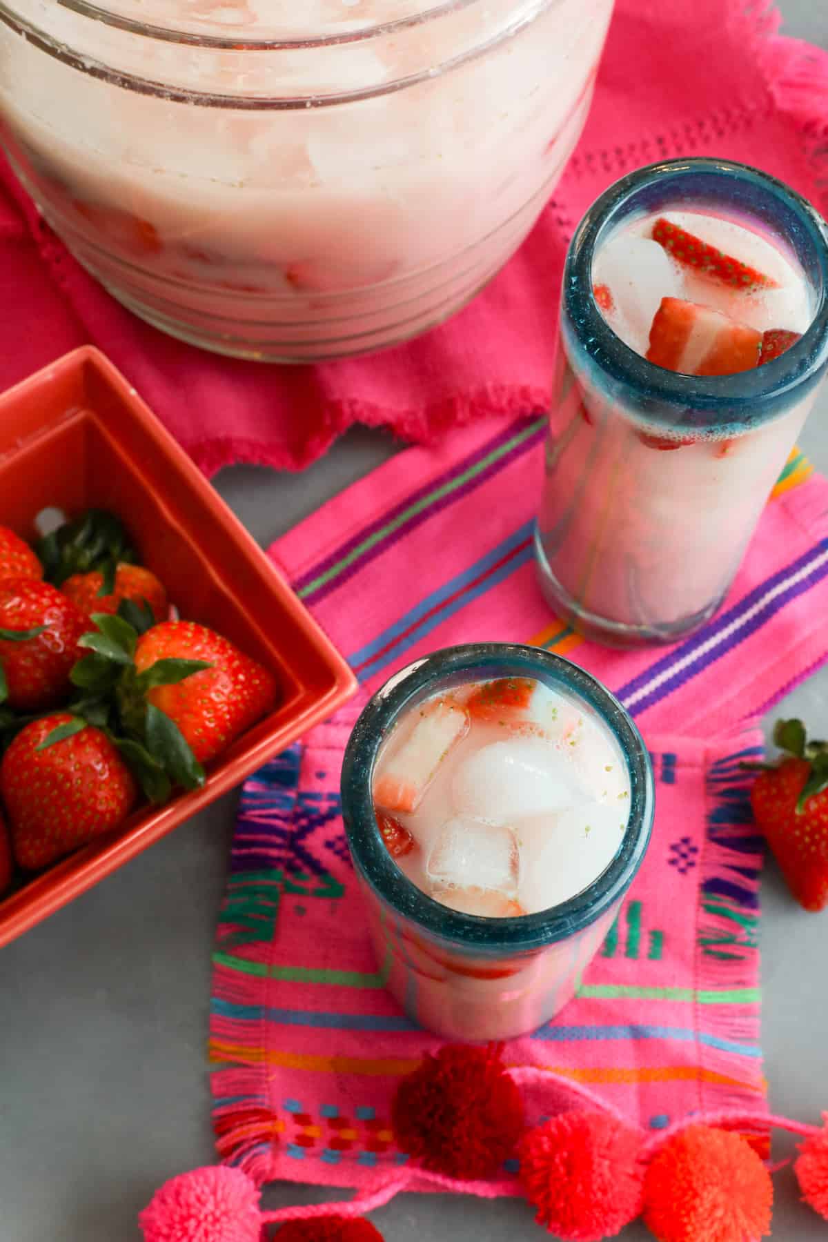 overhead shot of homemade strawberry horchata in glasses garnished with fresh strawberry slices on bright pink and blue striped fabric.