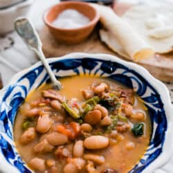 Frijoles Charros (Cowboy Beans) in a blue talavera bowl with corn tortillas in the background.