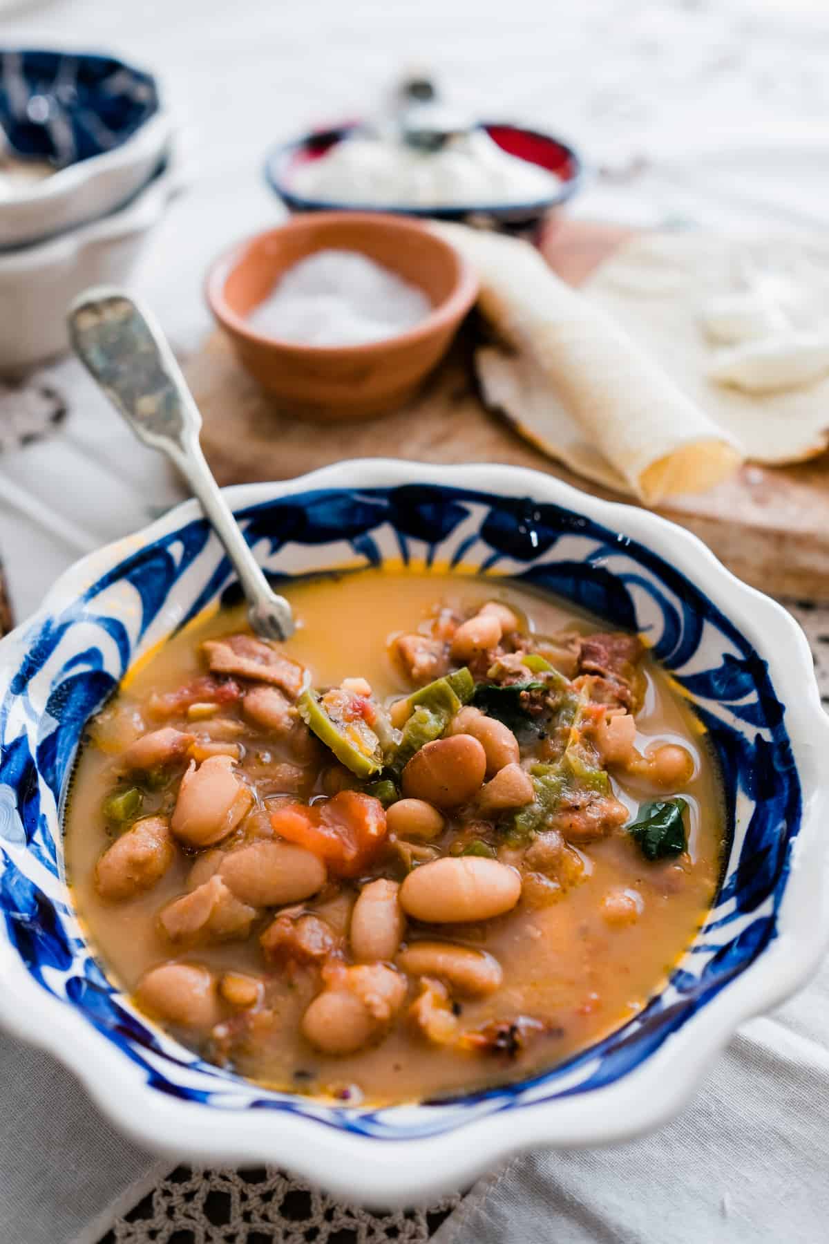 Frijoles Charros (Cowboy Beans) in a blue talavera bowl with corn tortillas in the background.