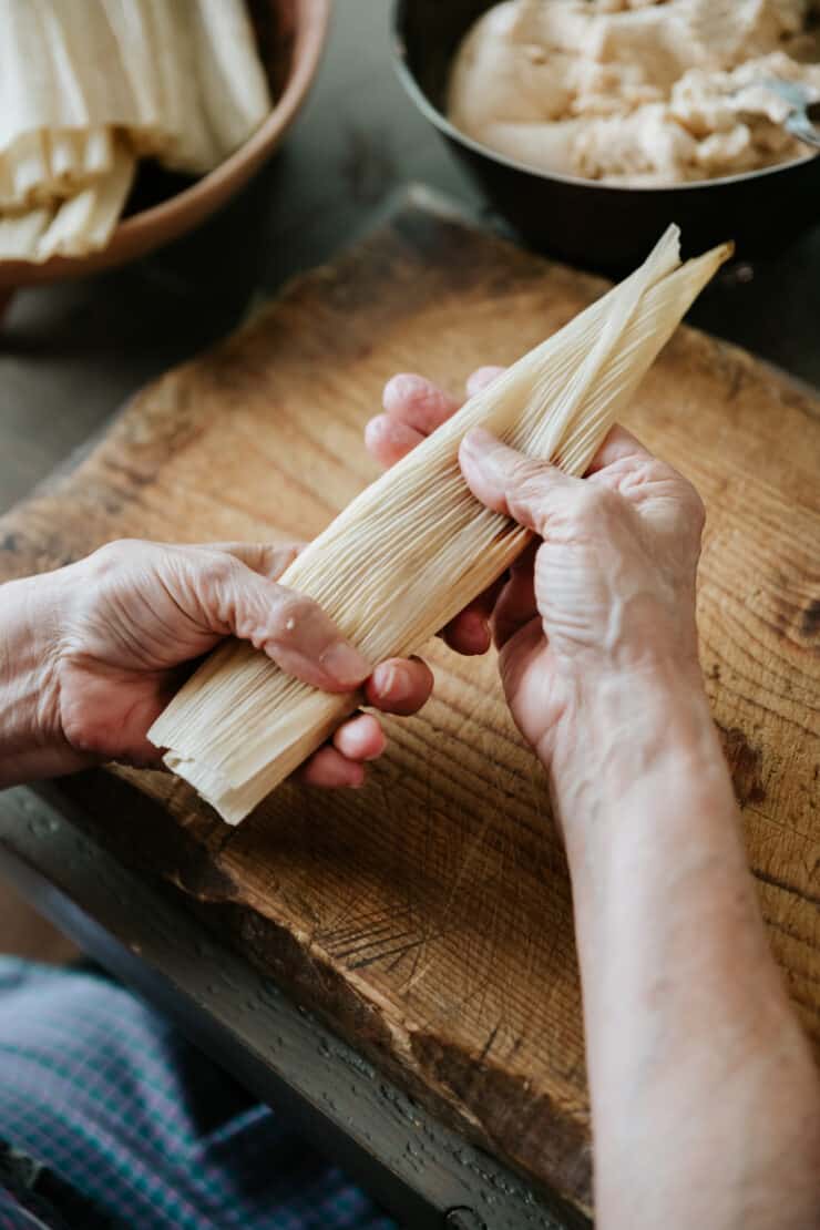 process shot, hands holding the pork tamal after the first set of folds. 