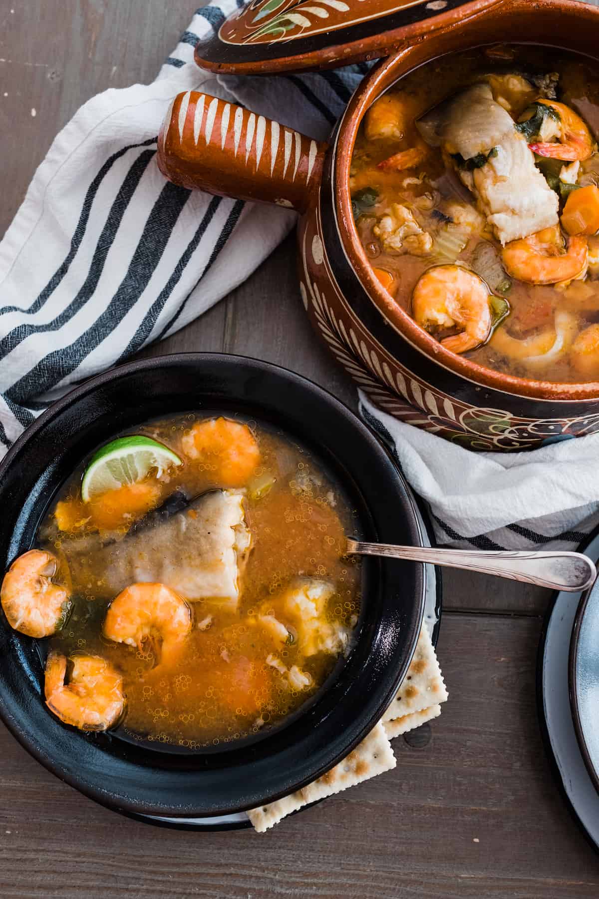 table with two bowls of caldo de camaron y pescado with a serving bowl of more Mexican fish soup.