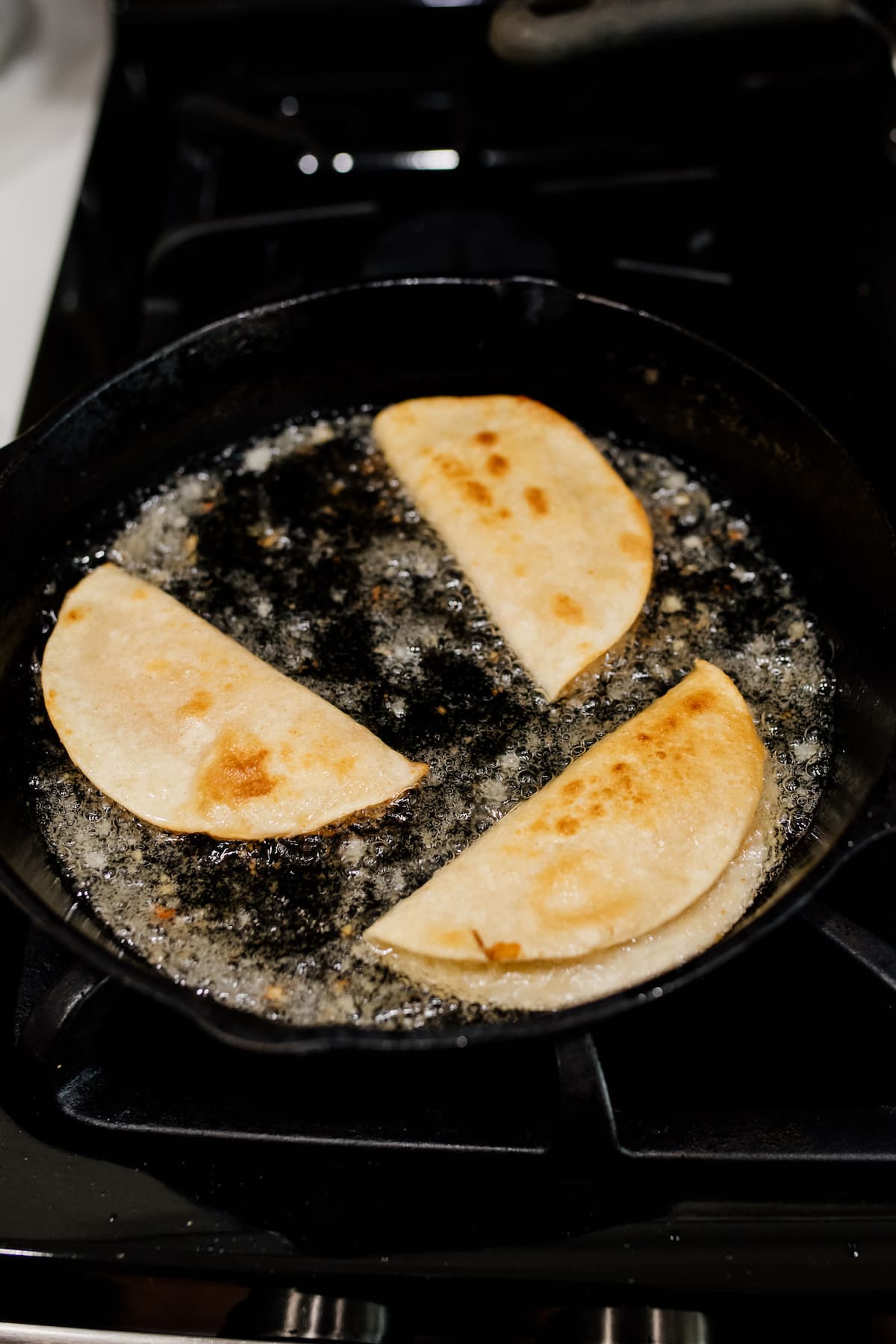vegetarian potato tacos being fried in a cast iron pan on stovetop.