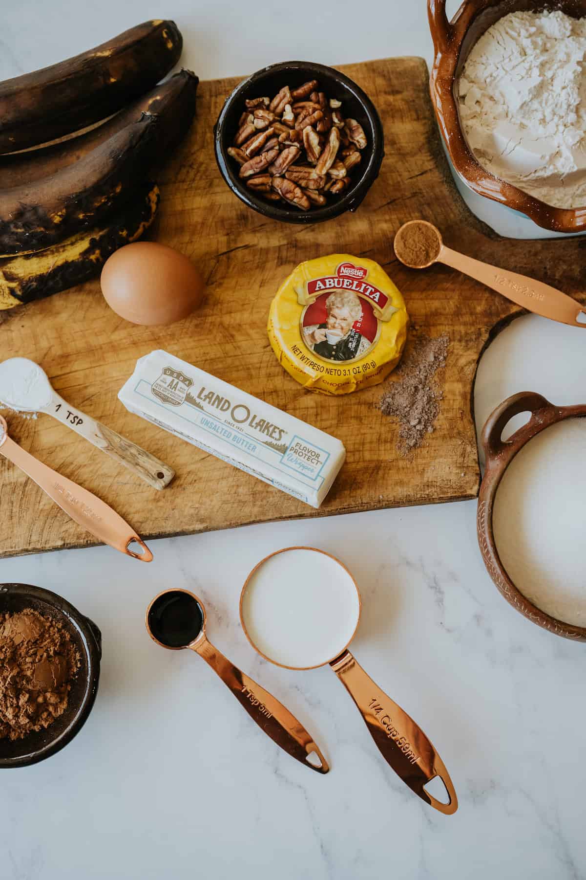 ingredients needed to make double chocolate banana bread with pecans and mexican chocolate measured out into bowls on a wooden cutting board. 