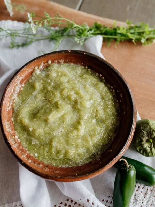 Barro brown Mexican pottery bowl filled with homemade Mexican salsa verde with jalapeño tomatillo and cilantro on the side.