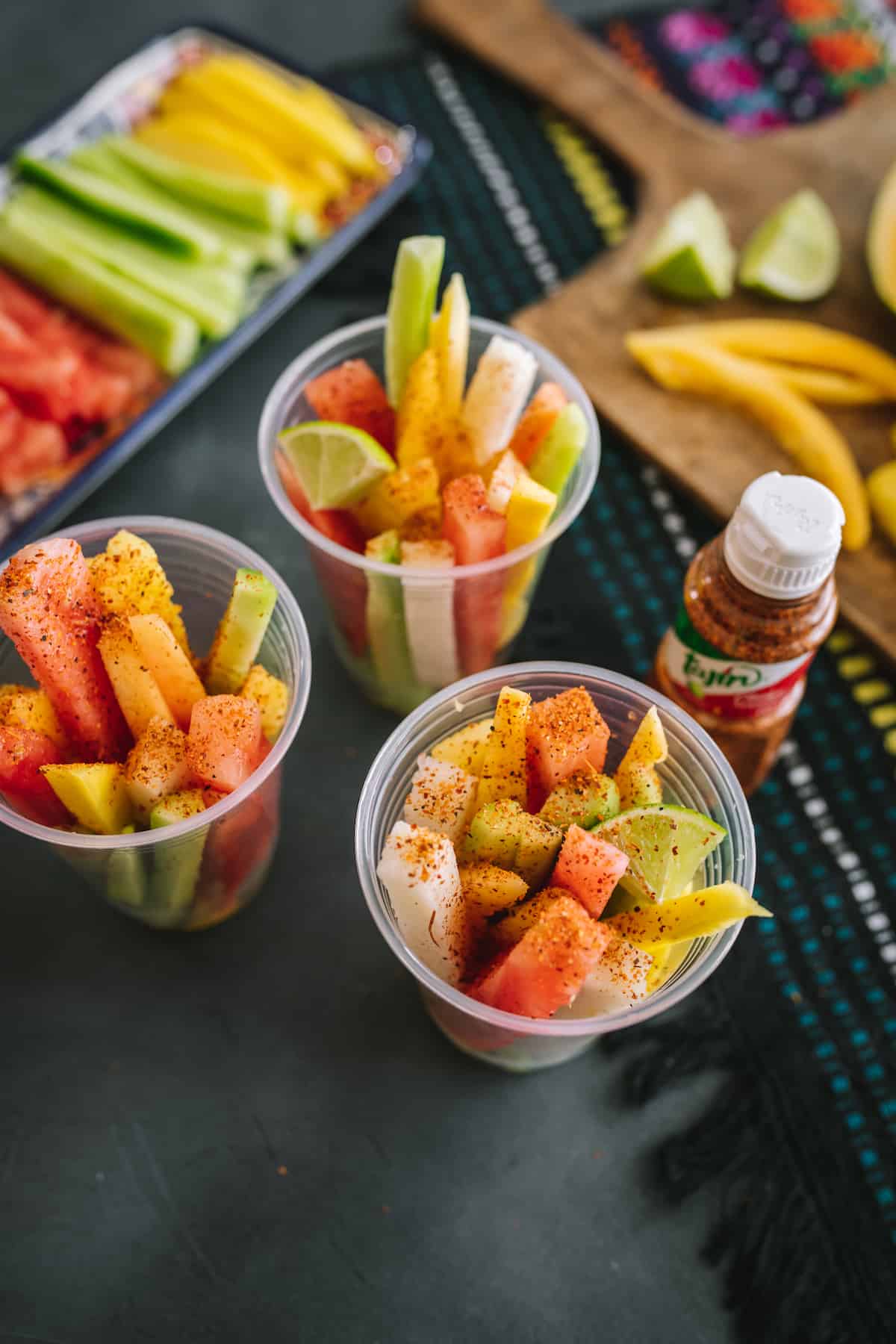 three plastic cups filled with spears of tropical fruit and sprinkled with Tajin.