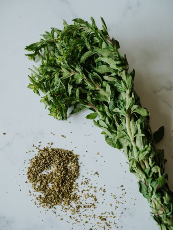 bundle of fresh mexican oregano and some dried mexican oregano on a white marble surface.