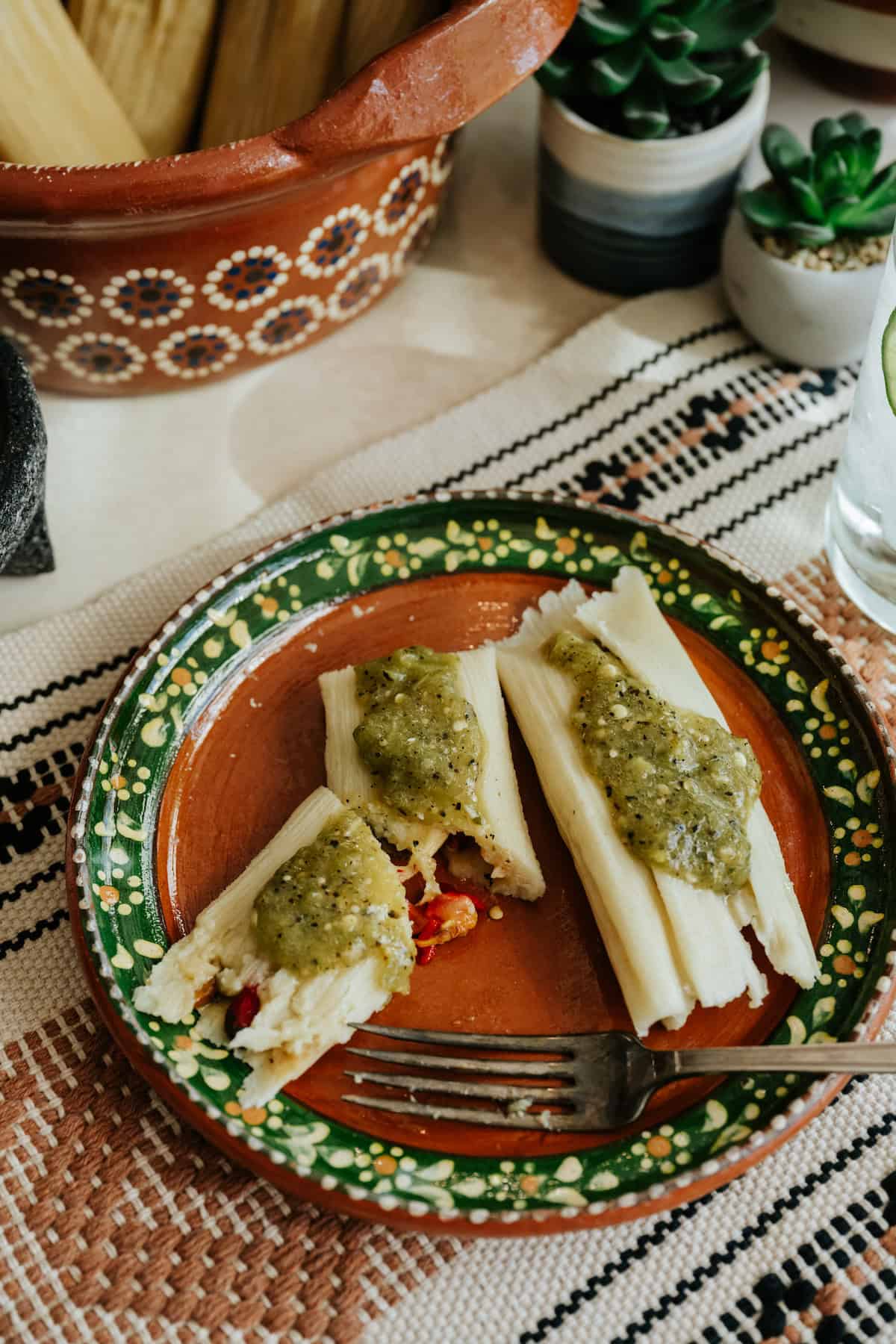 two cheese tamales topped with salsa verde on a hand-painted terracotta plate.
