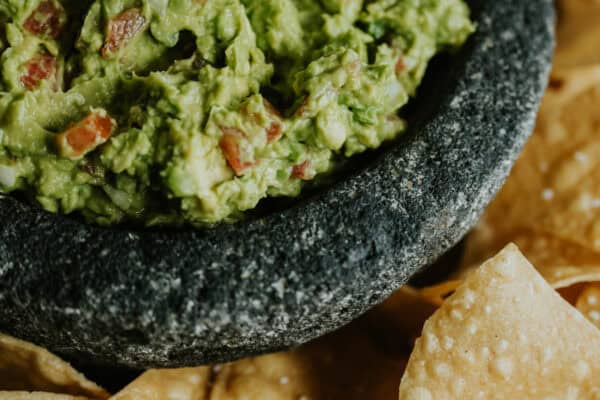 stone molcajete filled with chunky guacamole mexicano surrounded by tortilla chips.