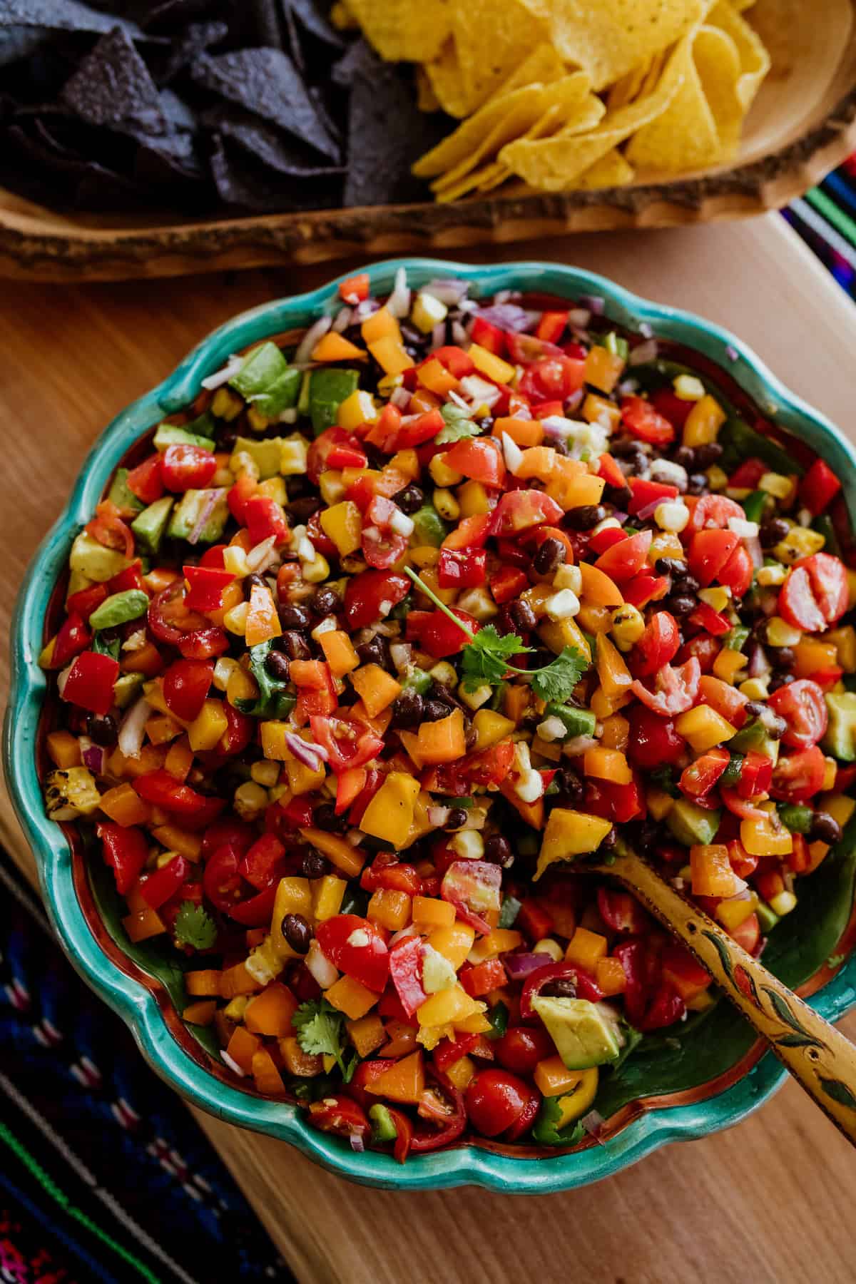 cowboy caviar in a teal bowl with wooden spoon served with blue and yellow corn chips.