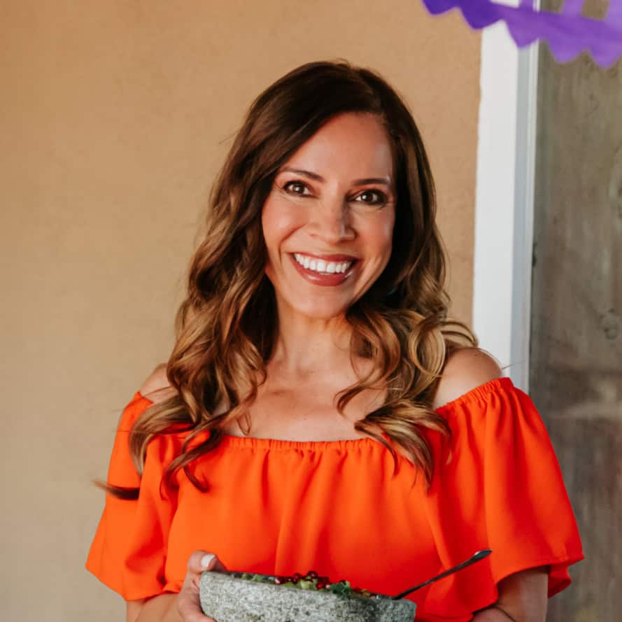 Yvette Marquez muy bueno Mexican food blogger in an orange dress holding a molcajete.