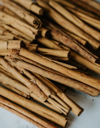 pile of Mexican cinnamon canela sticks on a white and grey marble table; there are some crumbs from the soft bark that have fallen around them.