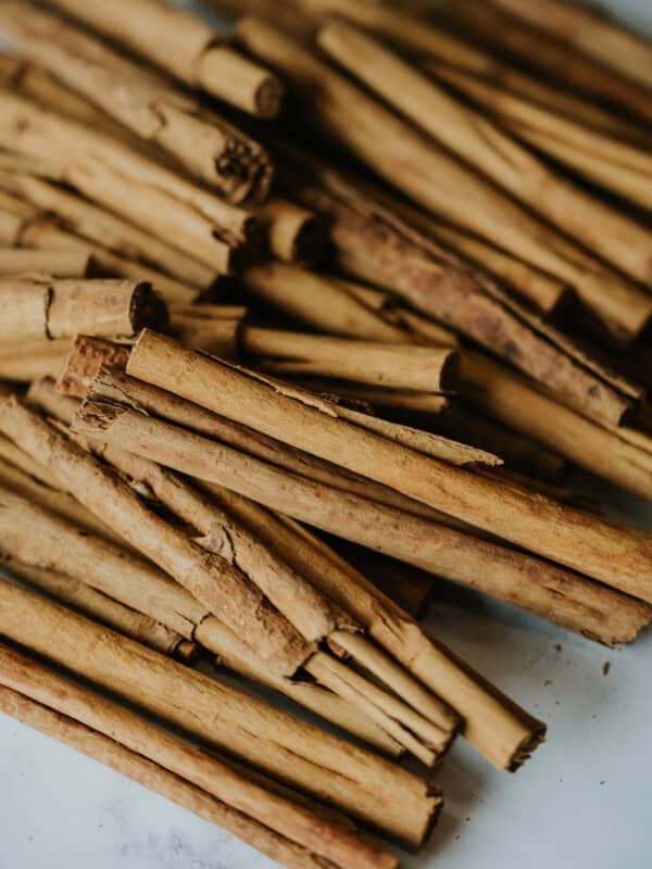 pile of Mexican cinnamon canela sticks on a white and grey marble table; there are some crumbs from the soft bark that have fallen around them.