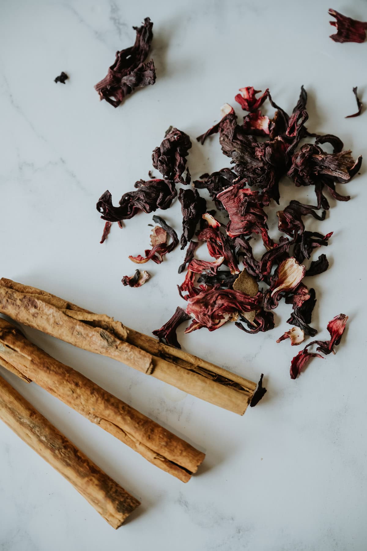 dried hibiscus flowers and canela sticks on a white table for making té de jamaica y canela. 