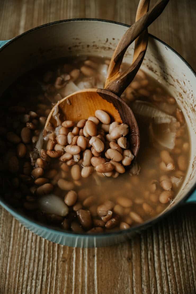 Frijoles de la olla in a dutch oven on a wooden table with a wooden servings spoon