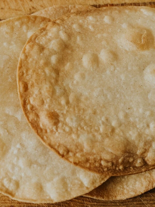 flat lay shot of three golden brown homemade tostada shells on a wooden surface.