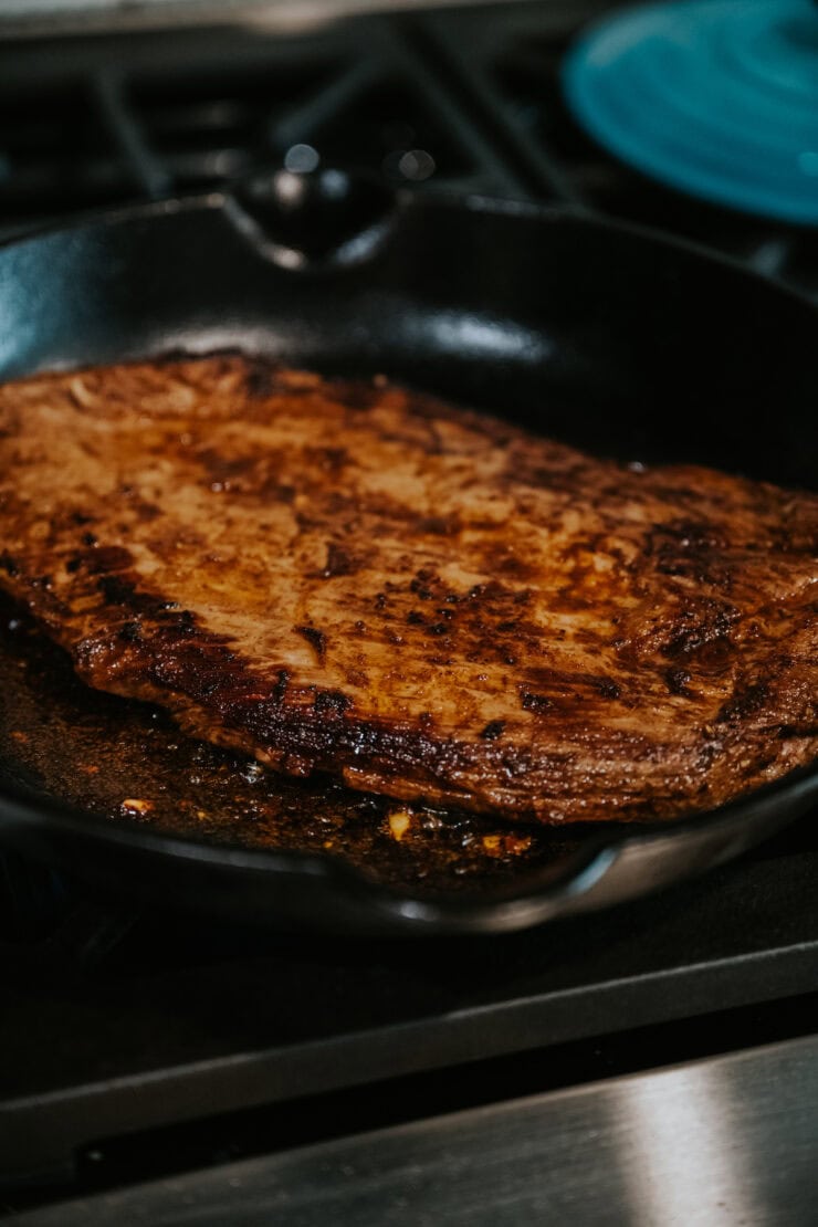 searing the marinated flank steak in a heated cast iron skillet. 