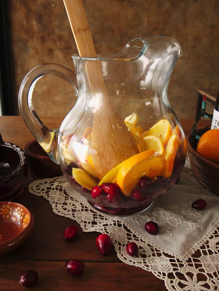 wooden spoon muddling orange slices on top of the cranberries. 