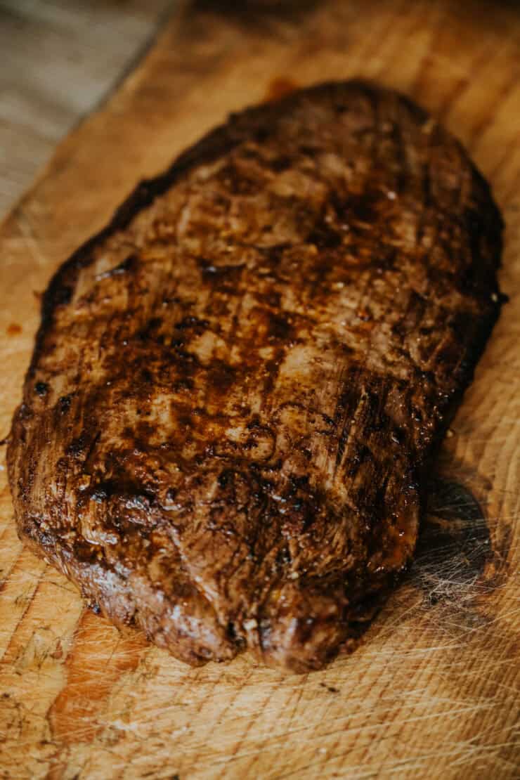 cooked whole flank steak resting on a wooden cutting board. 